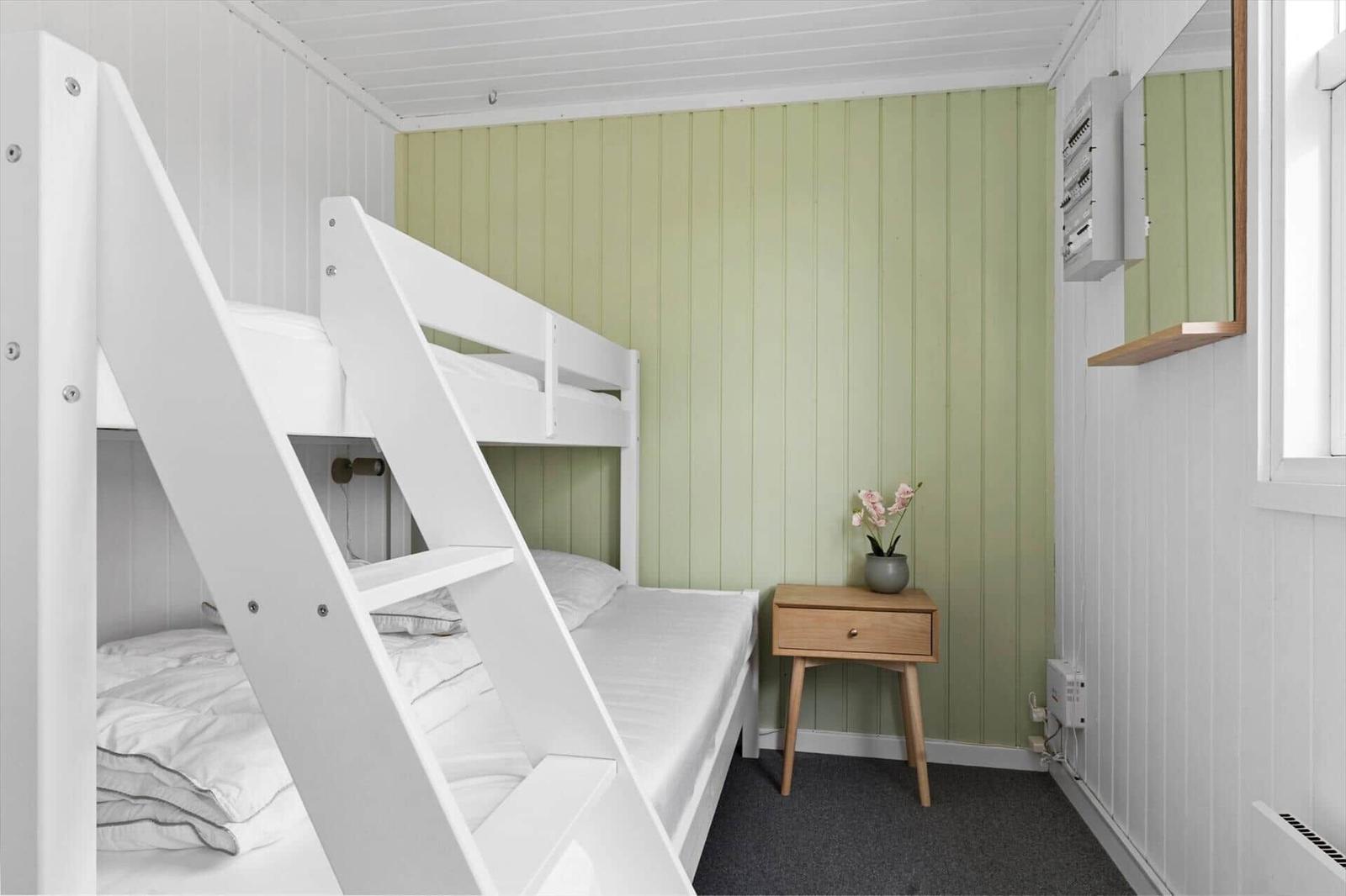 Zimmer mit Doppelstockbett, grüner Wand und kleinem Holztisch mit Blumen.