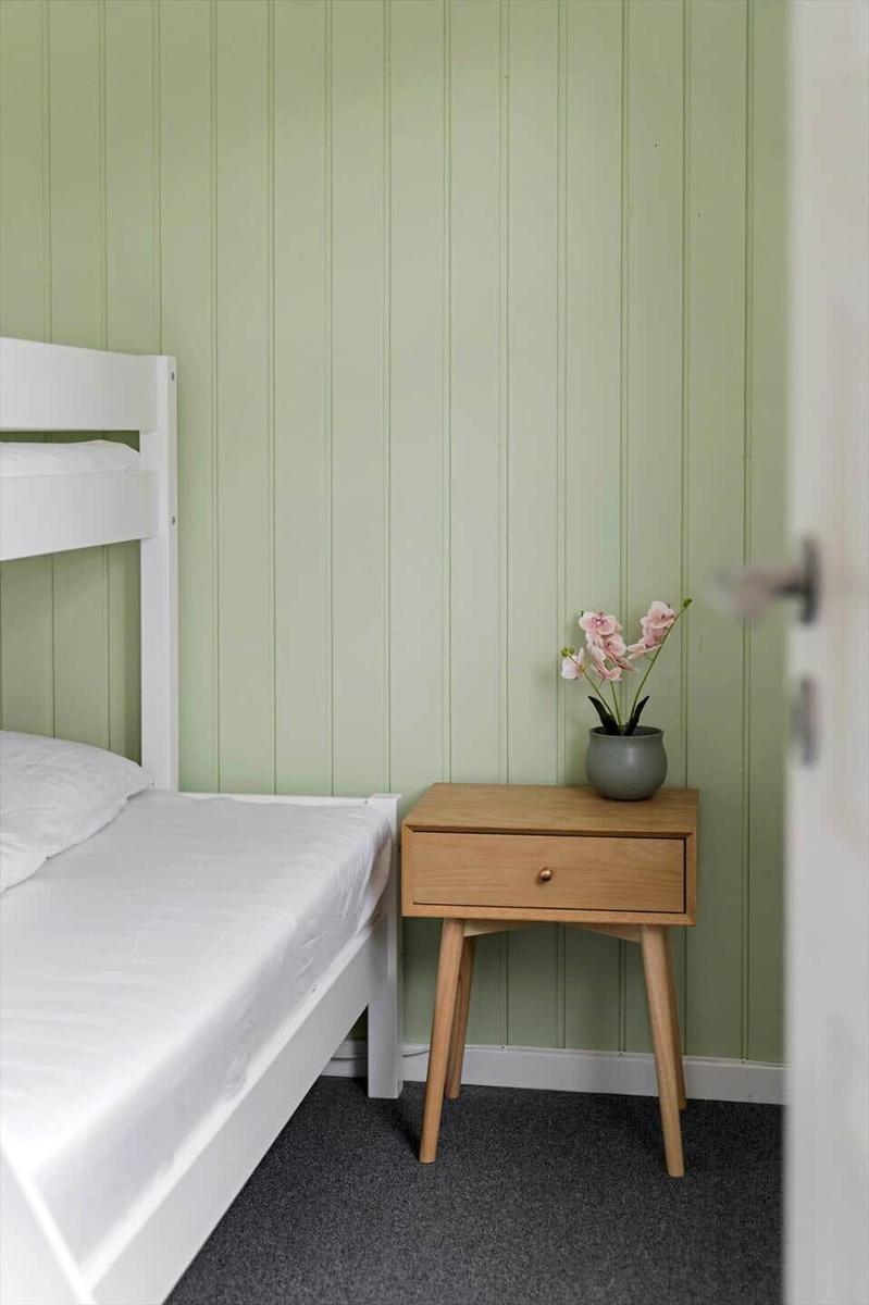 Ein Schlafzimmer mit einem weißen Bett und einem Holzhocker mit Blumen.