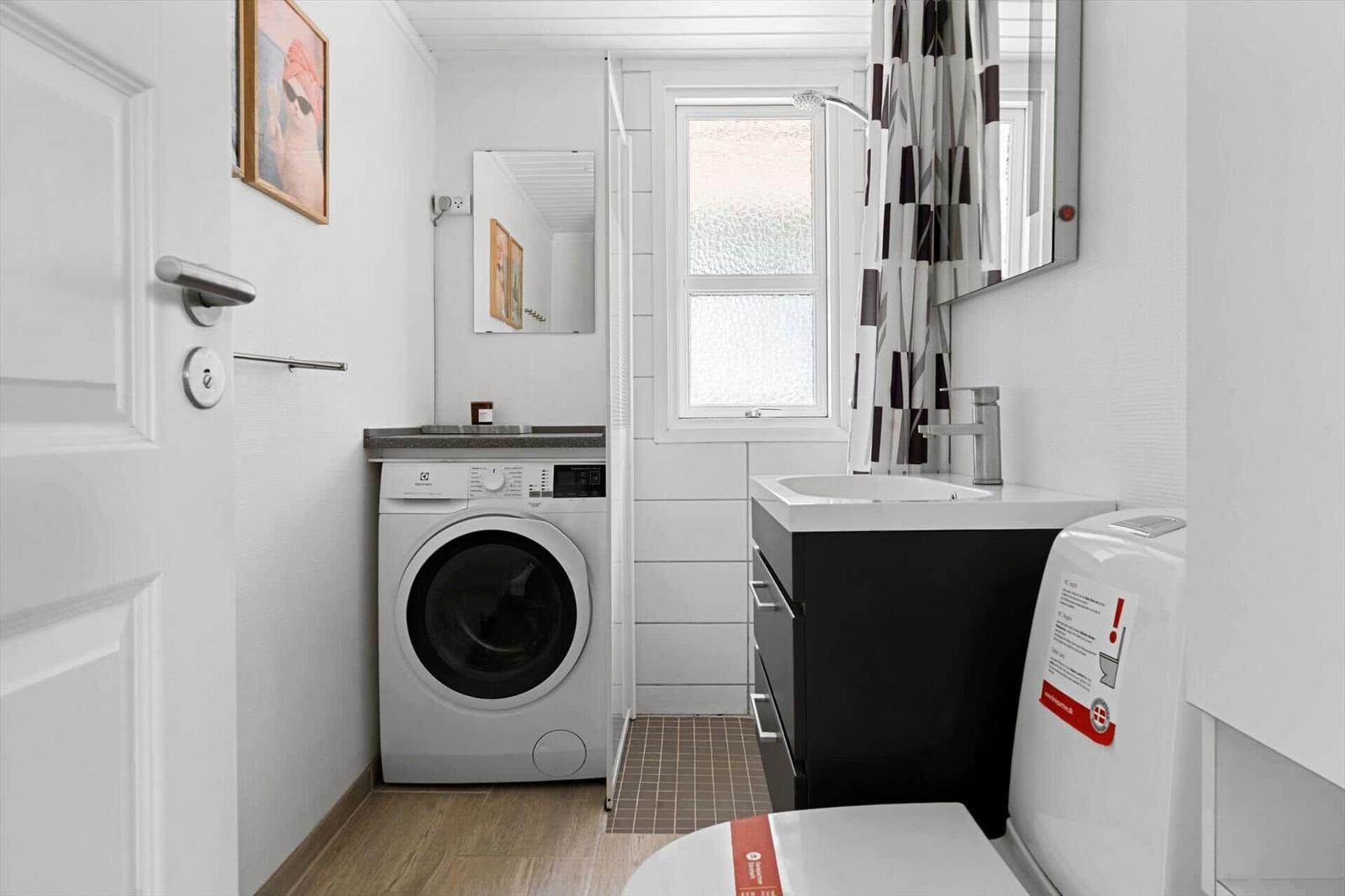 Badezimmer mit Waschmaschine, Waschbecken und Toilette. Fenster mit Duschvorhang.