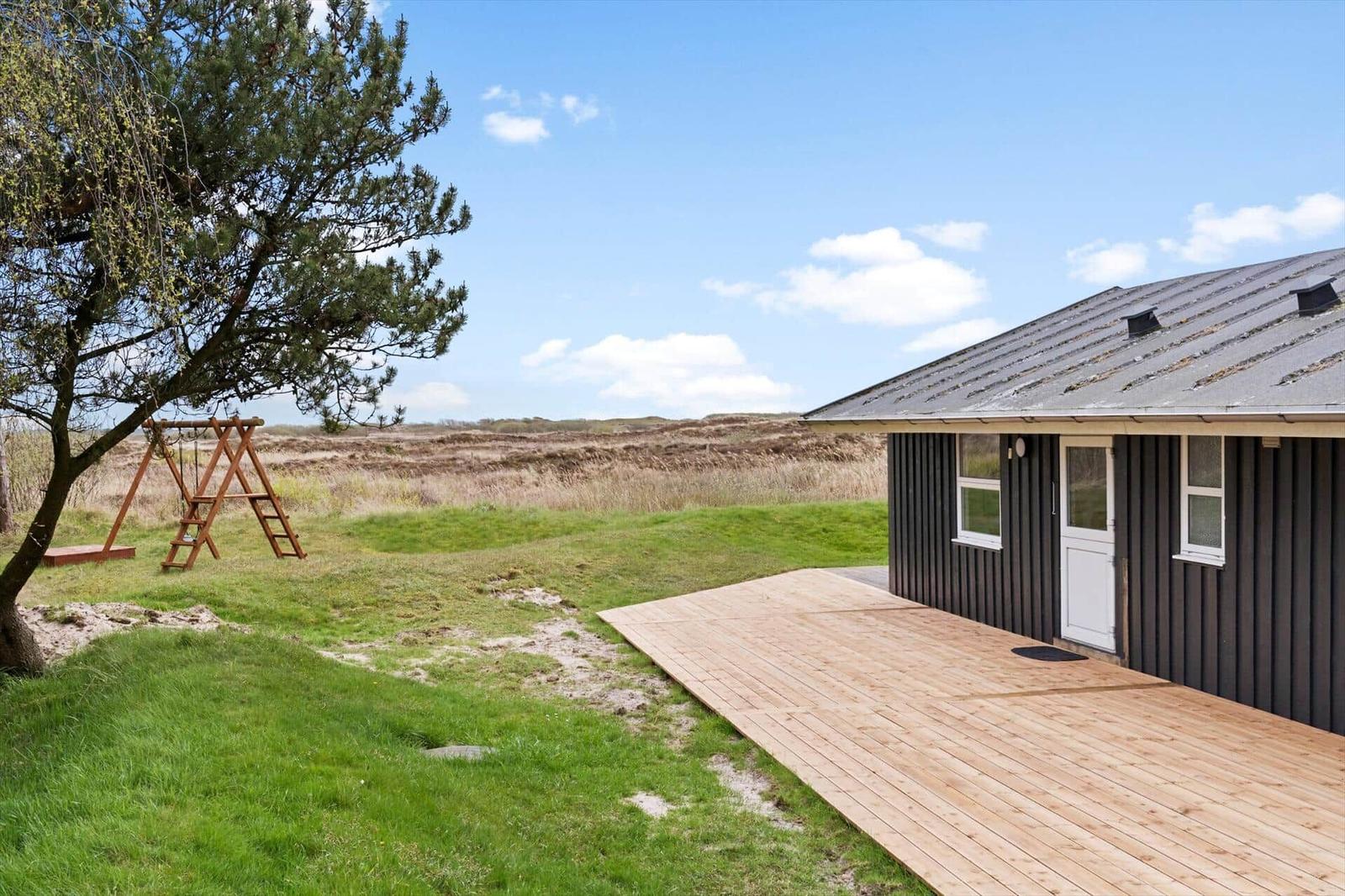 Haus mit Holzterrasse, Schaukel und Blick auf die Dünen.
