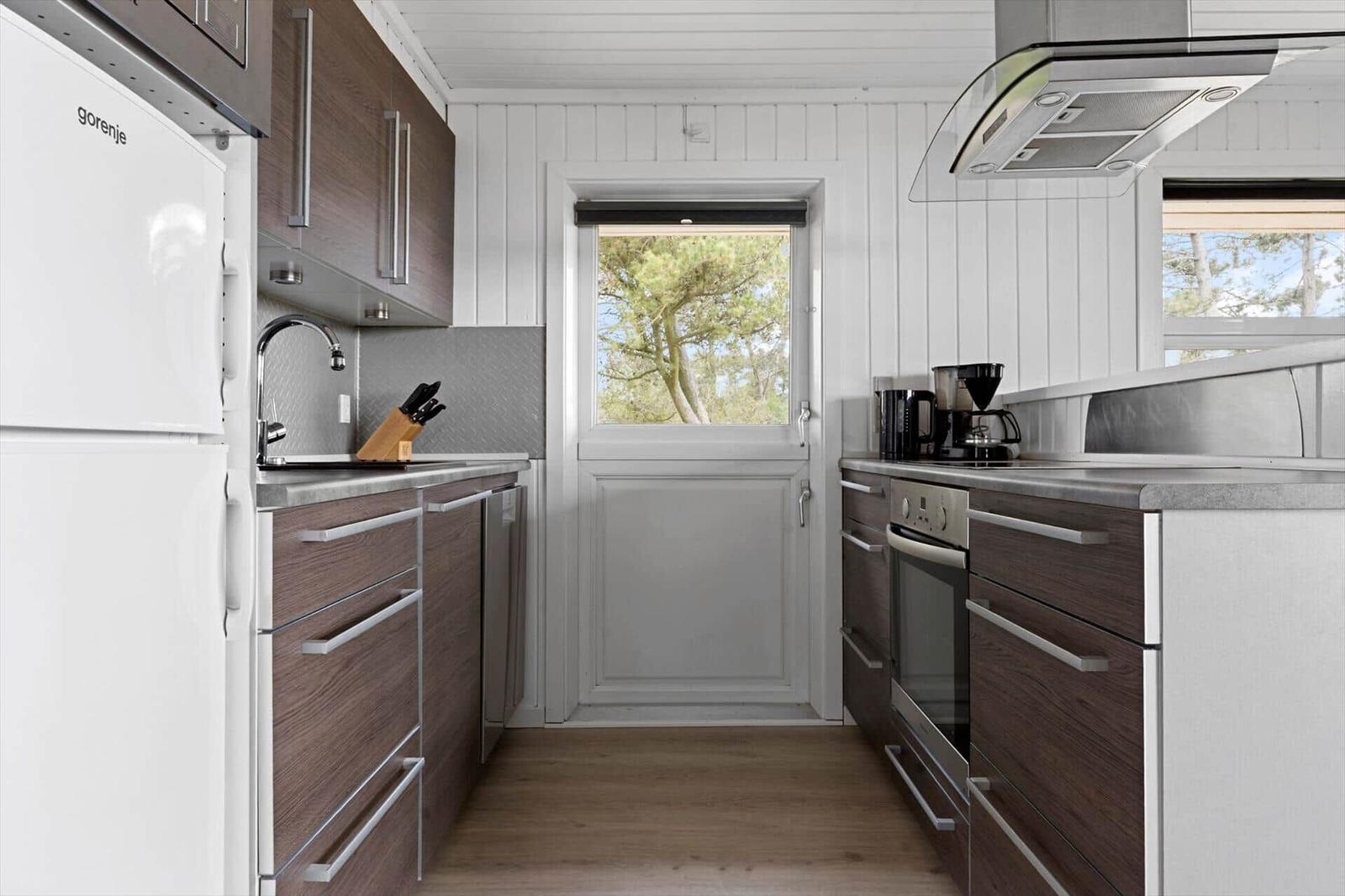Küche mit dunklen Schränken, weißer Kühlschrank und Blick auf einen Garten.