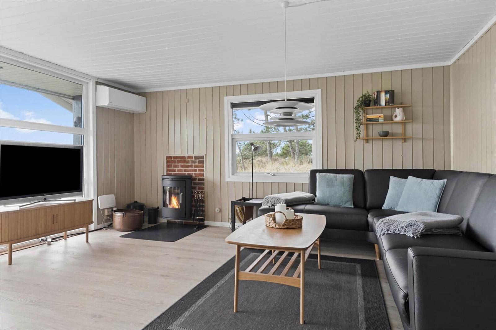 Wohnzimmer mit Sofa, Kamin und Fernseher. Holzboden und große Fenster.
