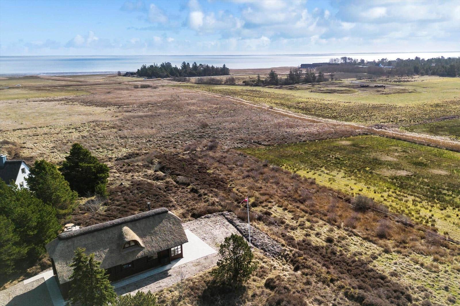 Haus mit Strohdach auf einer weiten Wiese, Blick auf Meer und Wald.