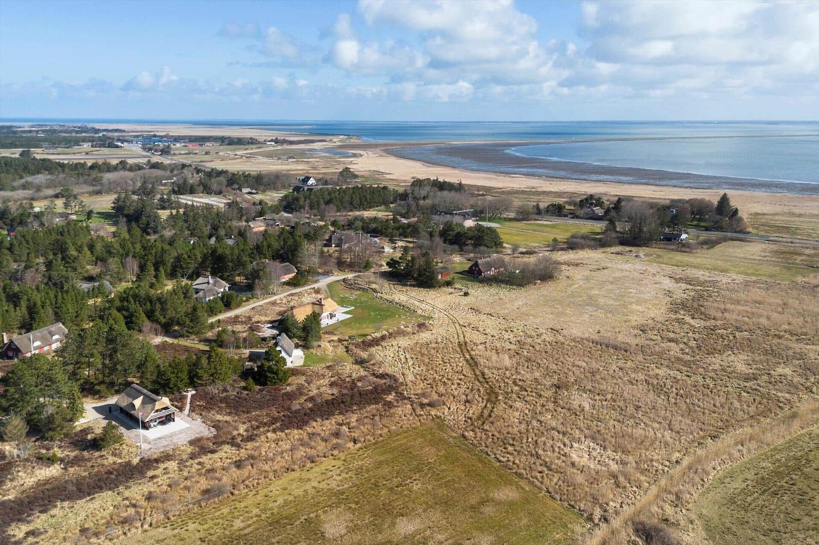 Aerielansicht einer ländlichen Gegend mit Häusern, Wiesen und einem nahen Strand.