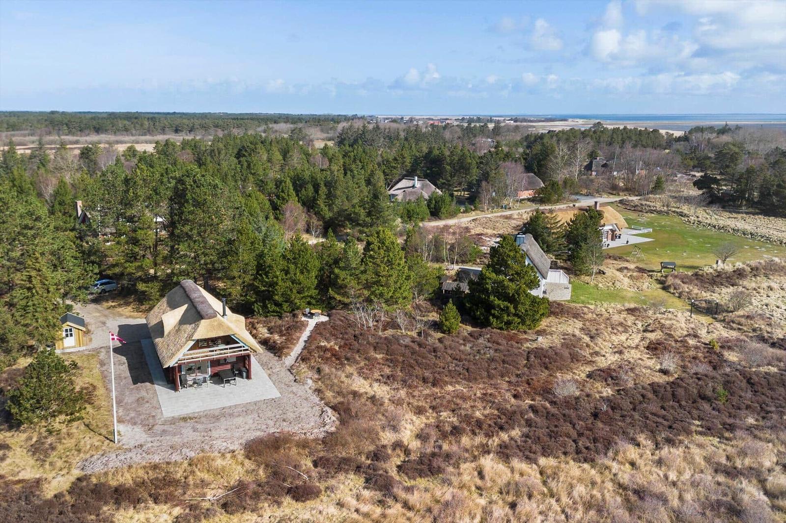 Hütte mit Strohdach in Waldlandschaft, Blick auf Meer und Grünflächen.