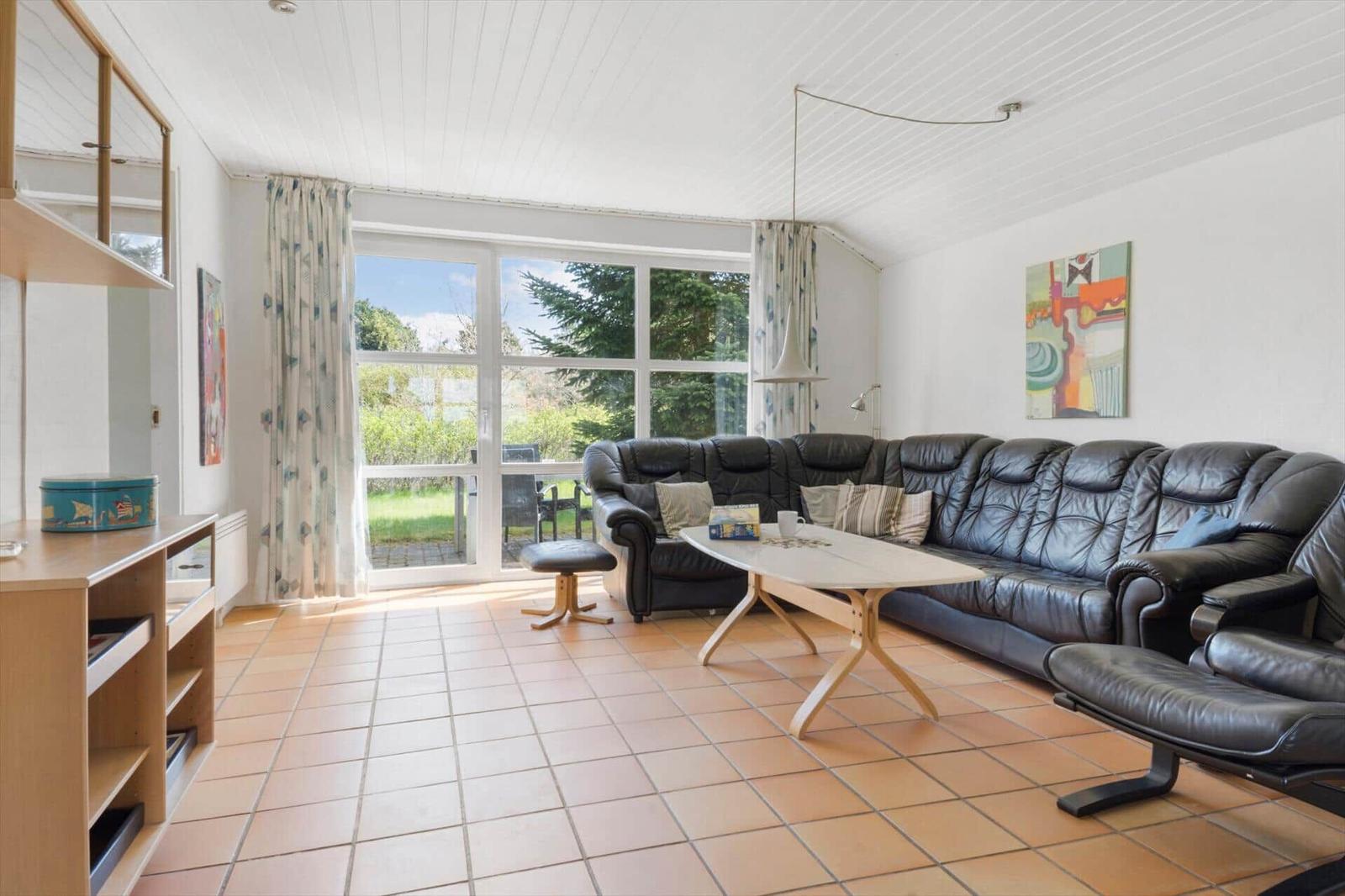 Wohnzimmer mit schwarzer Ledercouch, Holztisch und Terrassentür zum Garten.