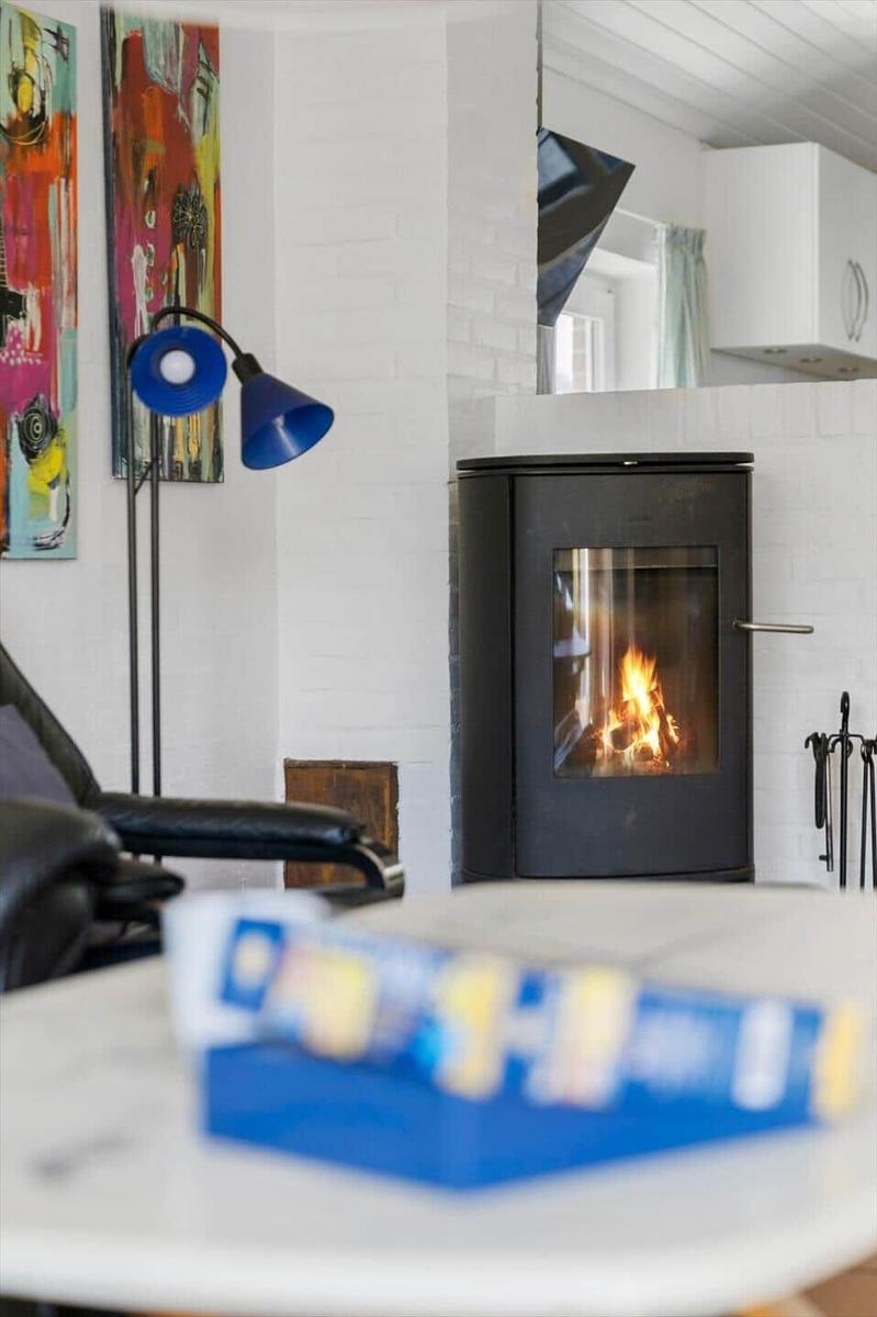 Ein Kamin mit brennendem Feuer, daneben eine blaue Stehlampe und Wandbilder.