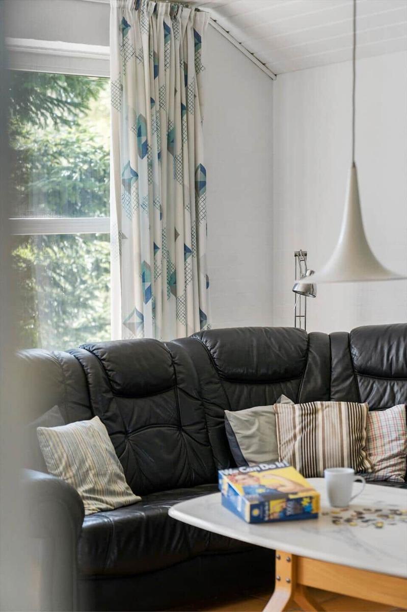 Schwarzes Sofa mit Kissen, Tisch mit Spiel und Tasse, Fenster mit Vorhängen.