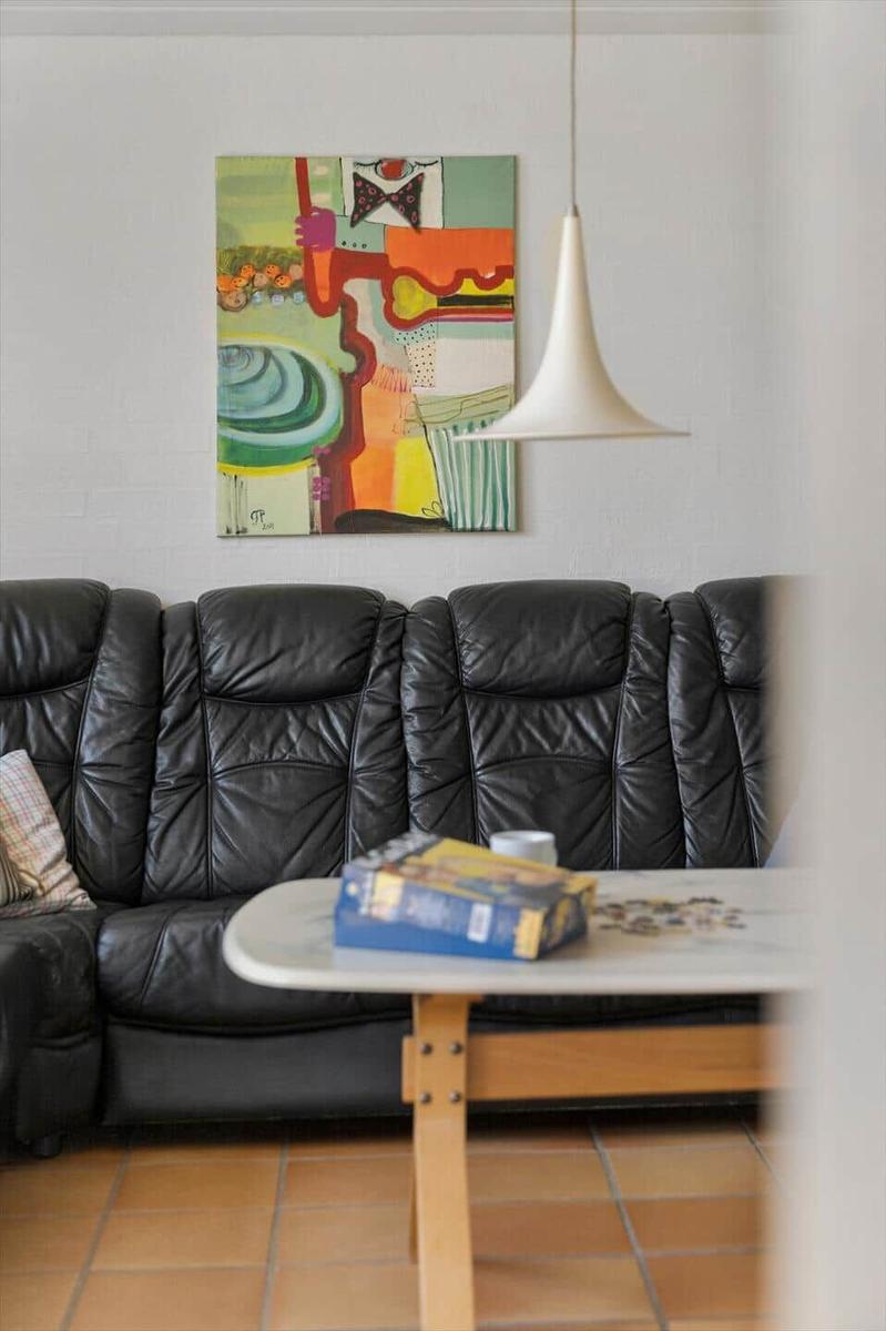 Schwarzes Ledersofa vor Wand mit abstraktem Gemälde und hängender Lampe.