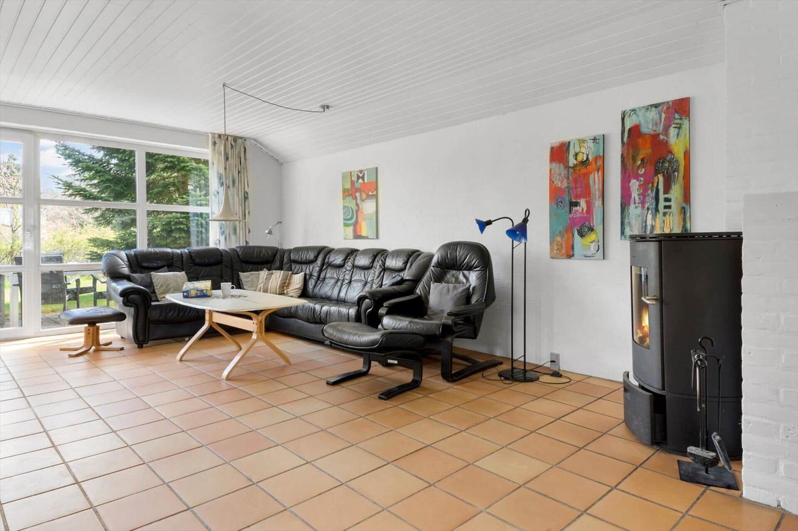 Wohnzimmer mit Ledersofa, Holztisch und Kaminofen. Fenster mit Blick auf Garten.