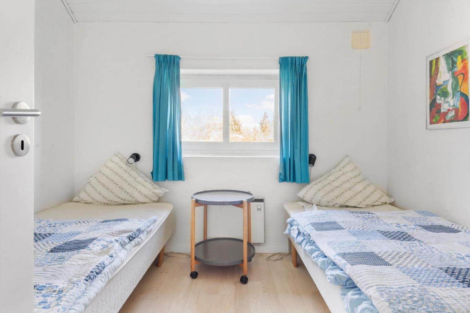 Zwei Betten mit blauen Decken, ein kleiner Tisch und ein Fenster mit blauen Vorhängen.