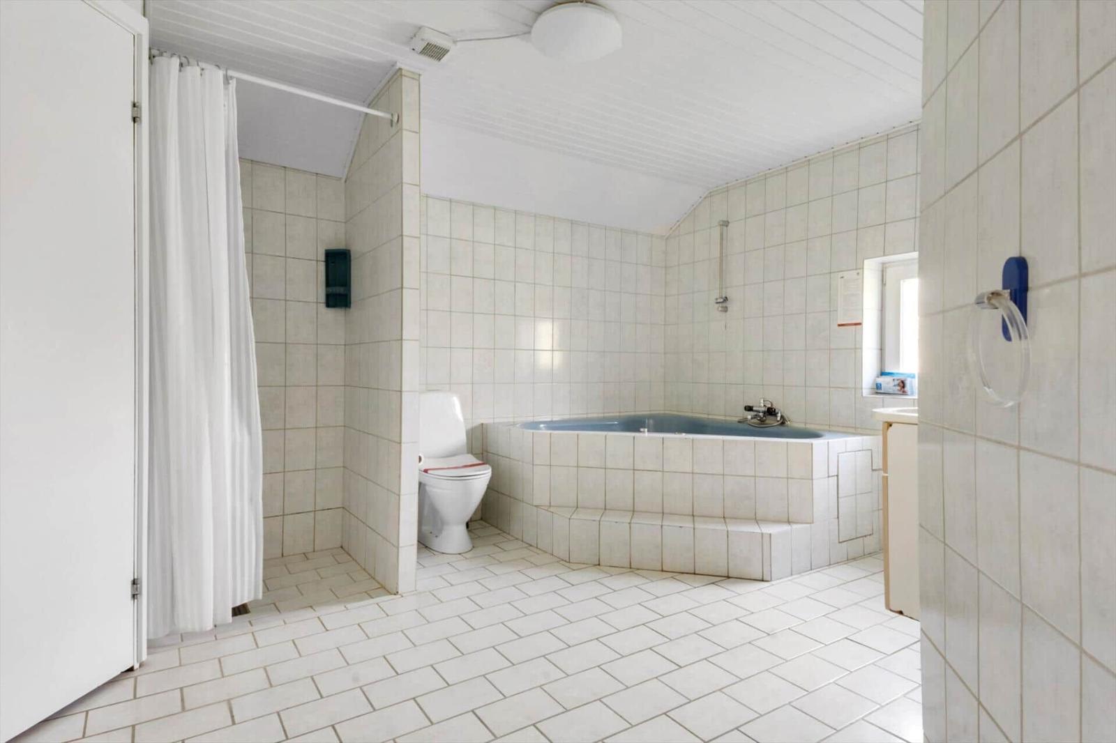 Bad mit Badewanne, Toilette und Dusche mit weißen Fliesen.