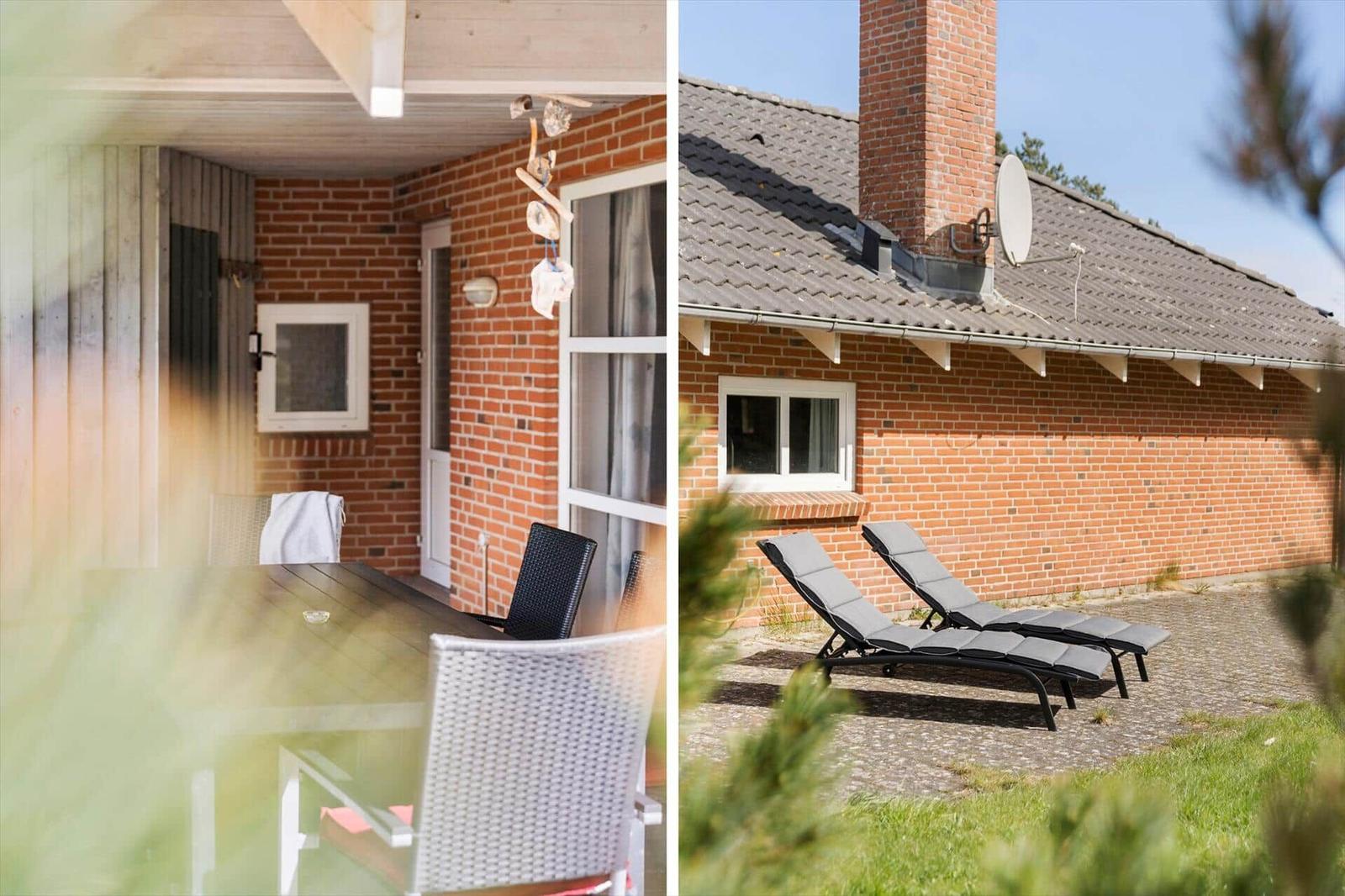Terrasse mit Tisch und Stühlen, daneben Garten mit Liegen und Backsteinhaus.