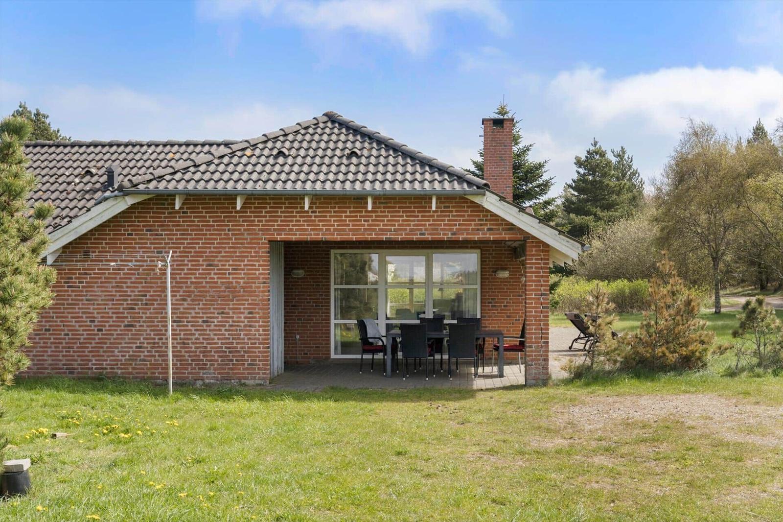 Ein Haus mit Terrasse, Tisch und Stühlen, umgeben von Gras und Bäumen.