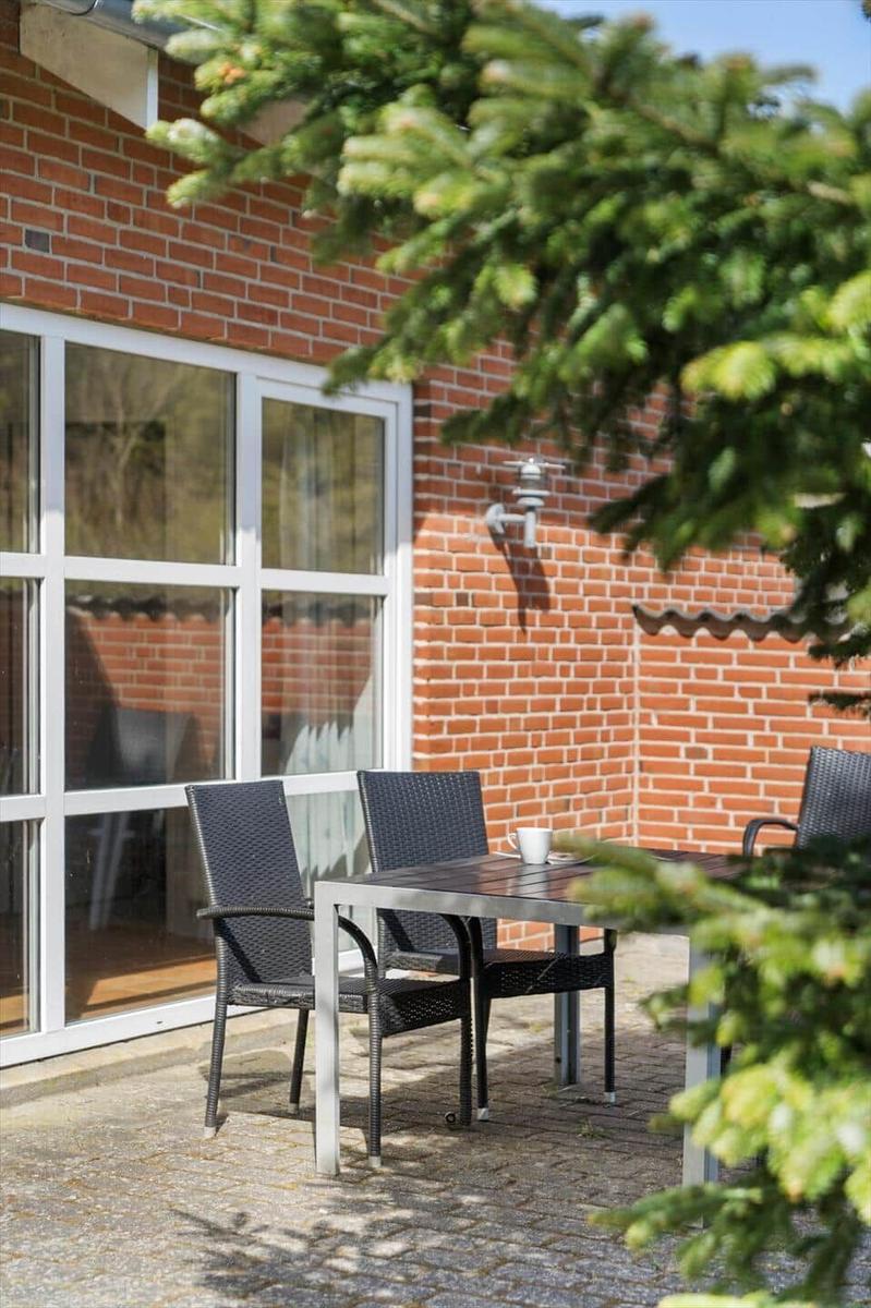 Außenbereich mit Tisch und Stühlen vor einer Backsteinwand mit großem Fenster.