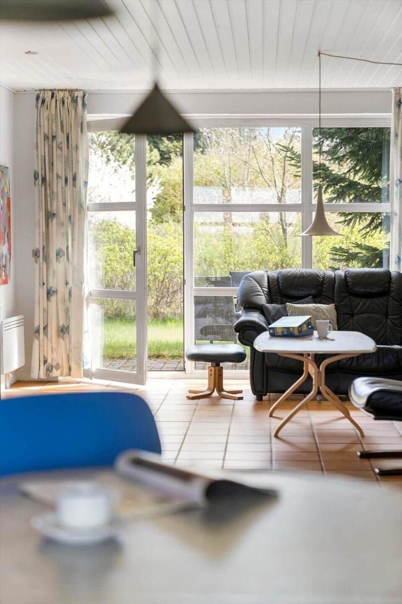 Wohnraum mit Sofa, Tisch und Blick auf Garten. Fenster und Tür führen nach draußen.