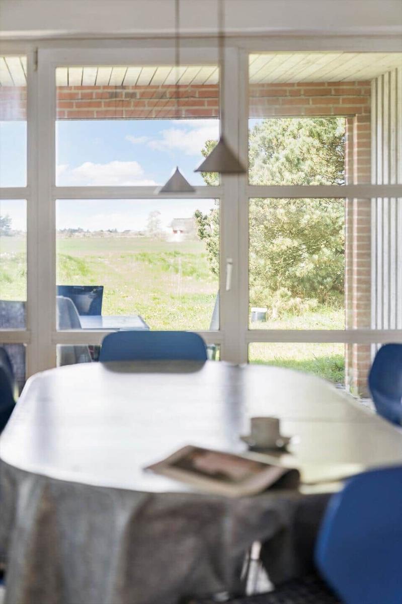 Essbereich mit Tisch und Stühlen, Blick auf Feld und Bäume durch große Fenster.