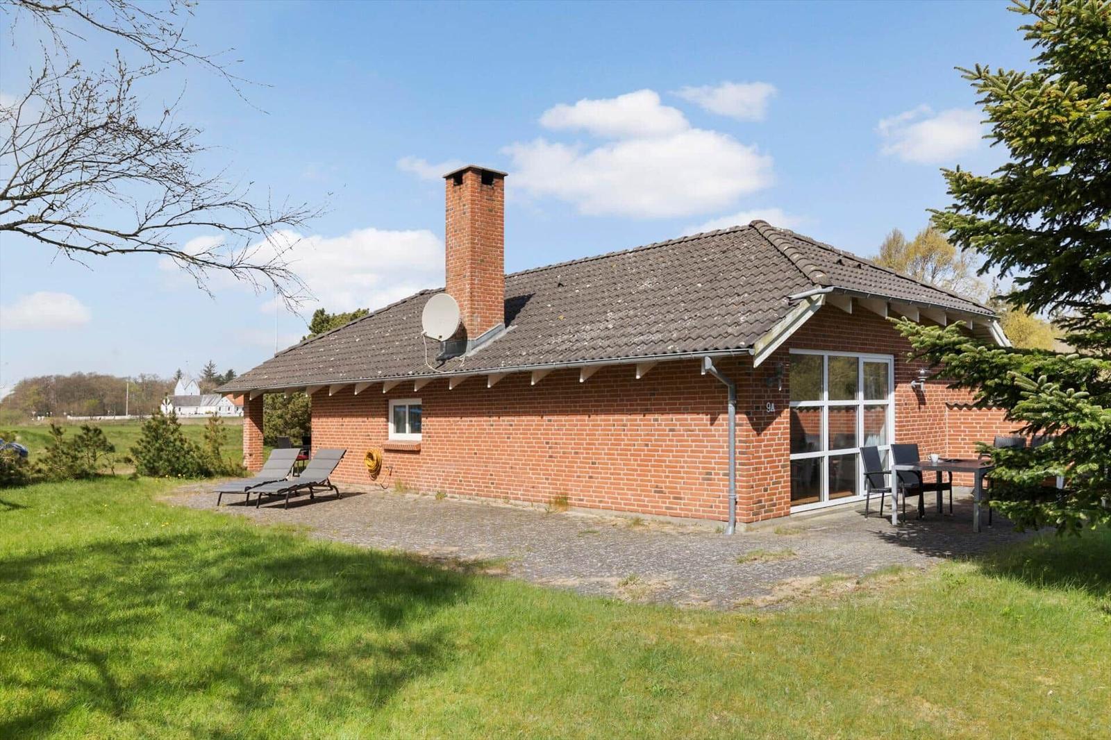 Rotes Backsteingebäude mit Terrasse, Liegen und Grillplatz im Garten.