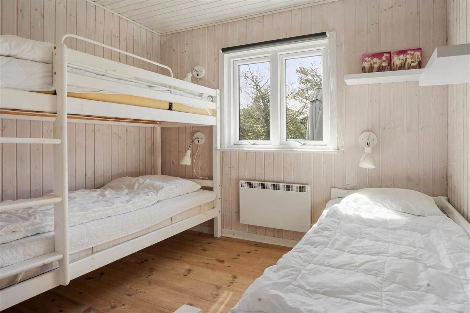 Zimmer mit Doppelstockbett und Einzelbett, Holzwand und Fenster.