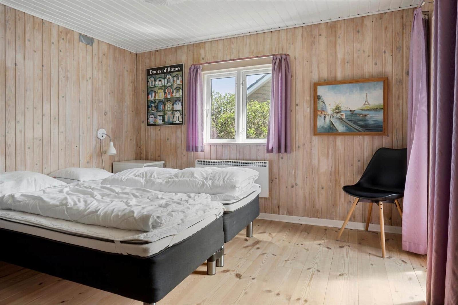 Zimmer mit zwei Betten, Holzwand, Fenster, Stuhl und Wandbild.
