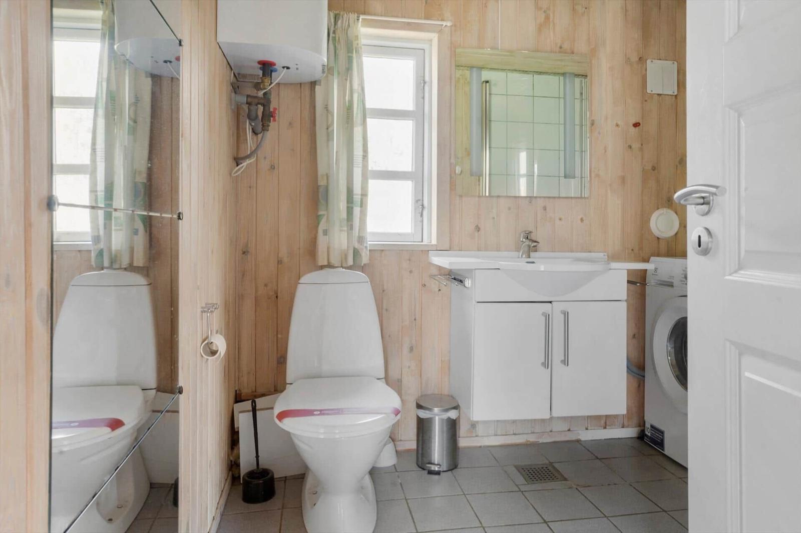 Badezimmer mit Toilette, Waschbecken und Waschmaschine. Holzwand und Fenster.