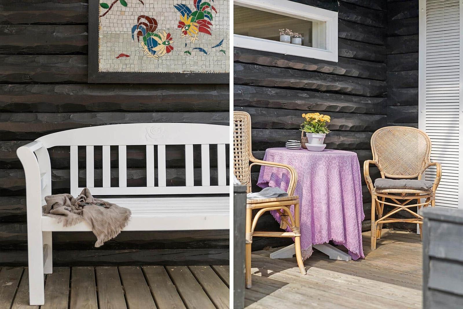 Weiße Bank mit Decke vor Holzwand. Tisch mit Stühlen und Blumen auf Terrasse.