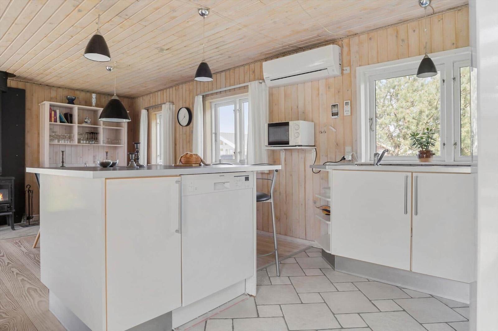 Küche mit weißen Schränken, Holzwand und -decke, Spüle, Mikrowelle und Waschmaschine.