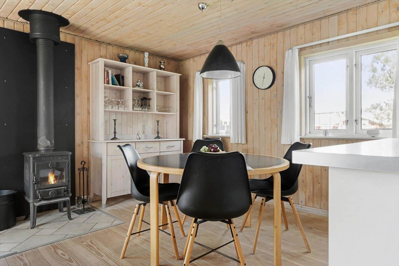 Esszimmer mit Holzwand, Esstisch, Stühlen und Kaminofen.
