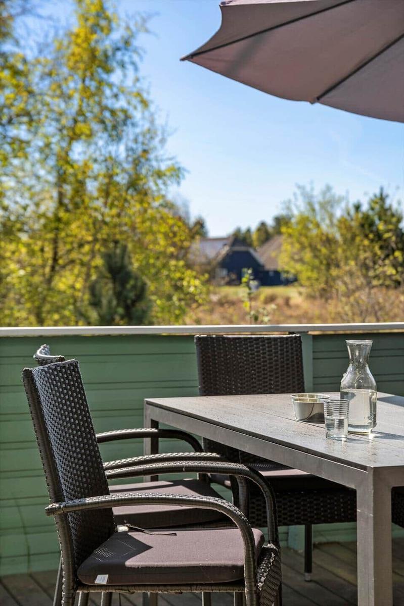 Terrasse mit Tisch, Stühlen und Sonnenschirm. Blick auf grüne Bäume und Ferienhaus im Hintergrund.