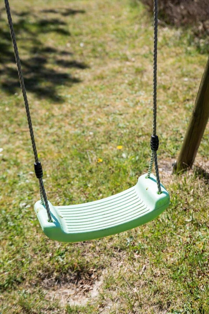 Ein grüner Schaukelstuhl hängt an Seilen im Garten.