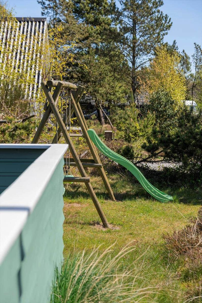 Grüner Rutschbereich und Schaukel im Garten mit Bäumen und Gras.