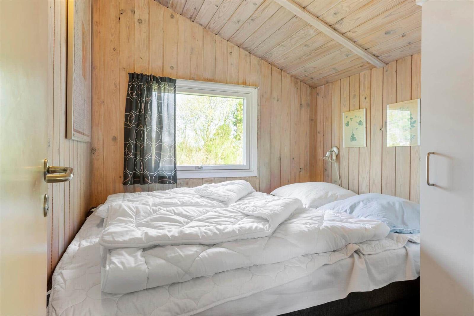 Schlafzimmer mit Holzwand, Bett und Fenster mit Vorhang.