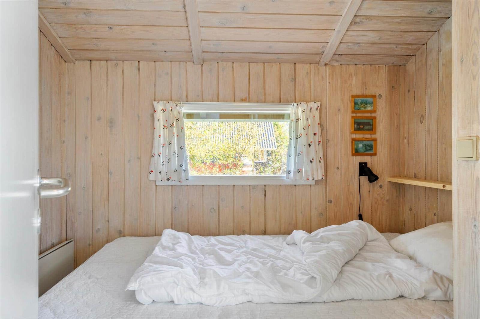Schlafzimmer mit Holzwand, Bett und Fenster mit Vorhängen.