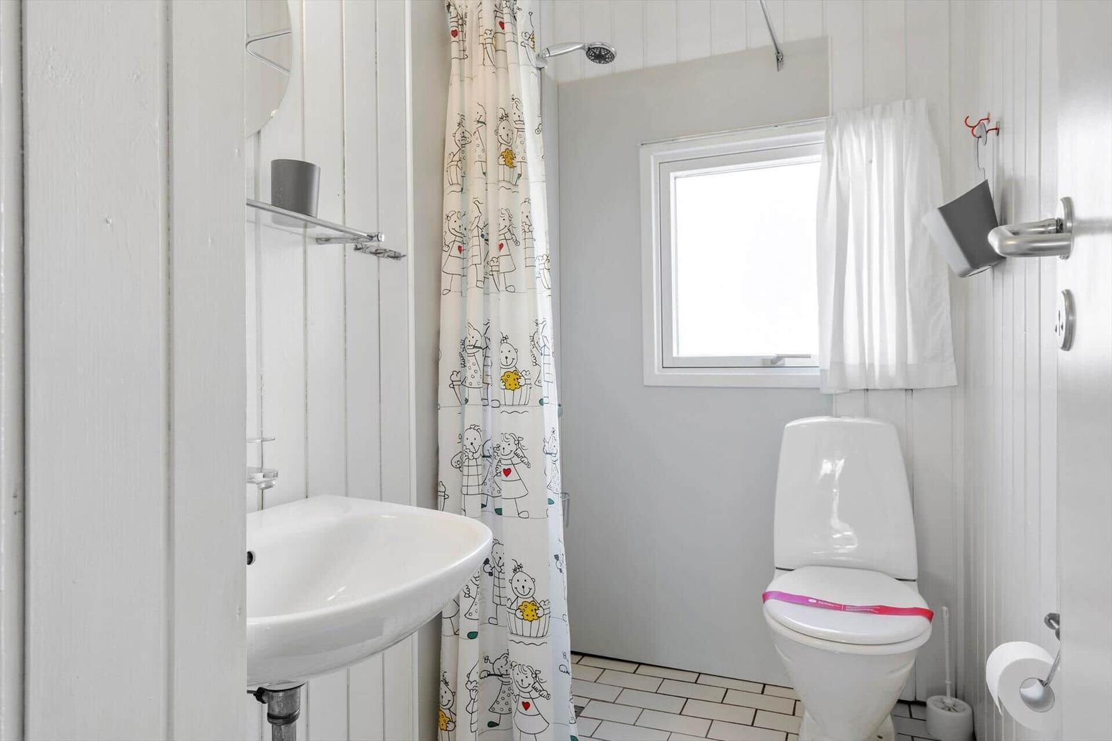 Badezimmer mit Dusche, Toilette und Waschbecken. Fenster mit Vorhang. Duschvorhang mit Kindermotiven.