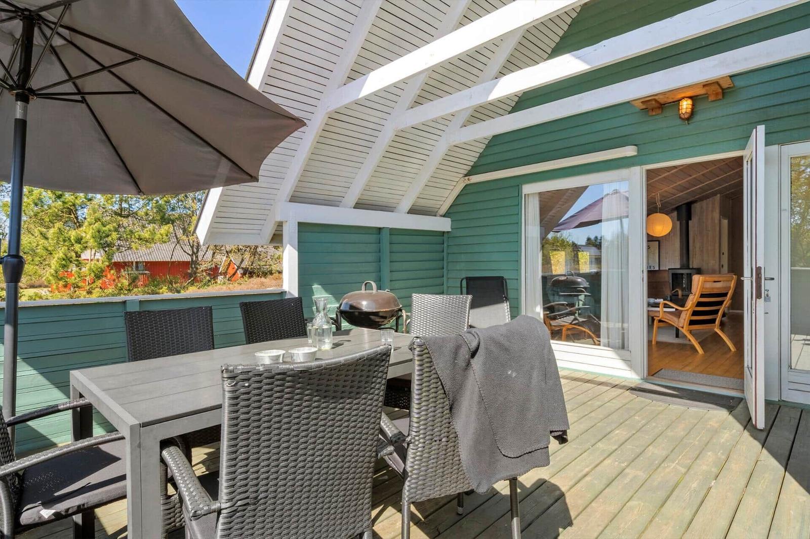 Terrasse mit Tisch, Stühlen und Sonnenschirm. Durch Glastüren ist Innenraum sichtbar.