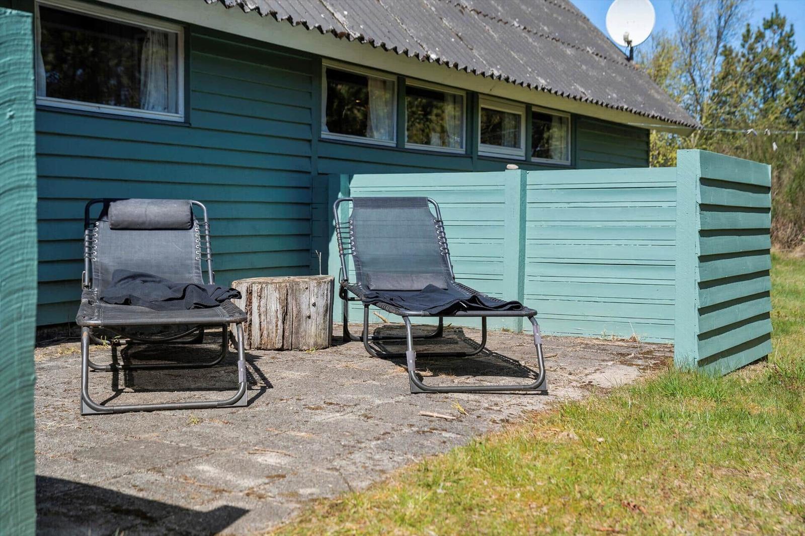 Zwei Liegestühle stehen vor einem Haus mit grünem Holzschindelverkleidung und Zaun.