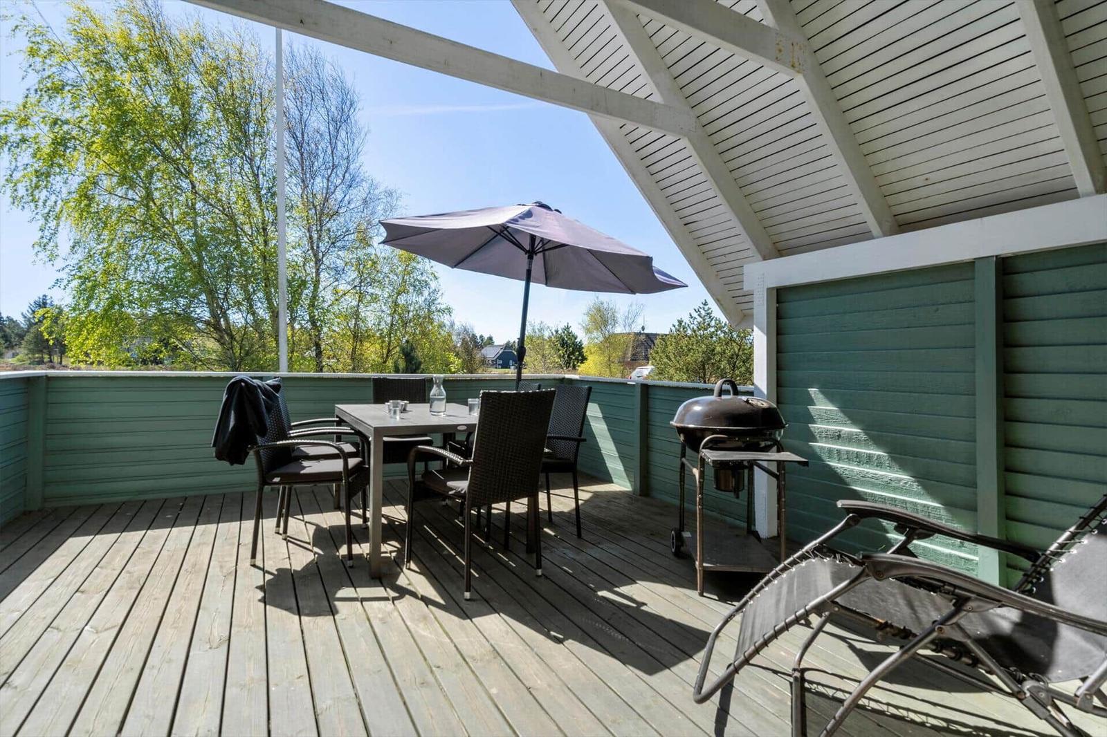 Terrasse mit Tisch, Stühlen, Sonnenschirm und Grill unter Dach.
