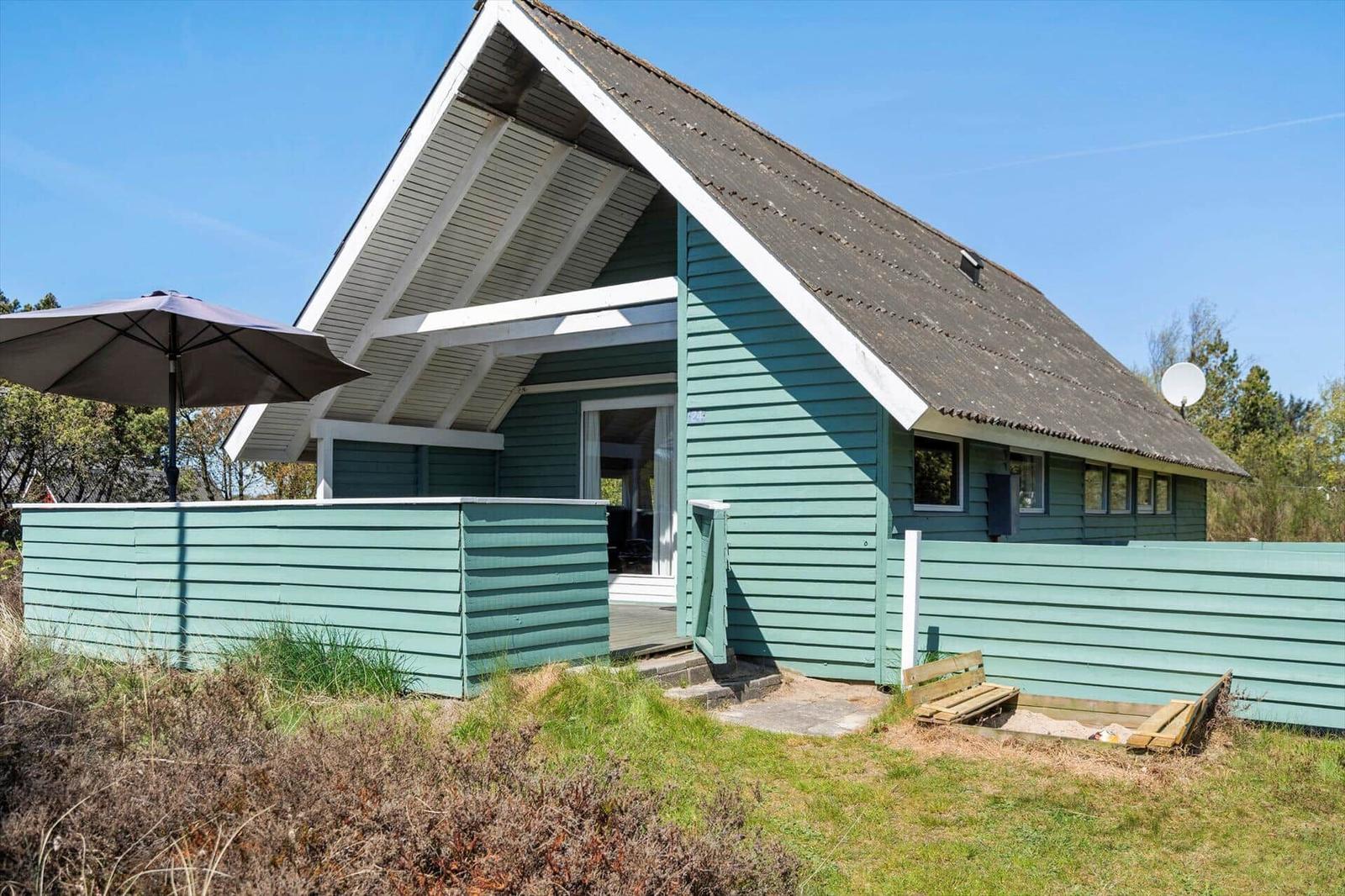Ein grünes Holzhaus mit Dachüberstand und Außenterrasse mit Sonnenschirm.