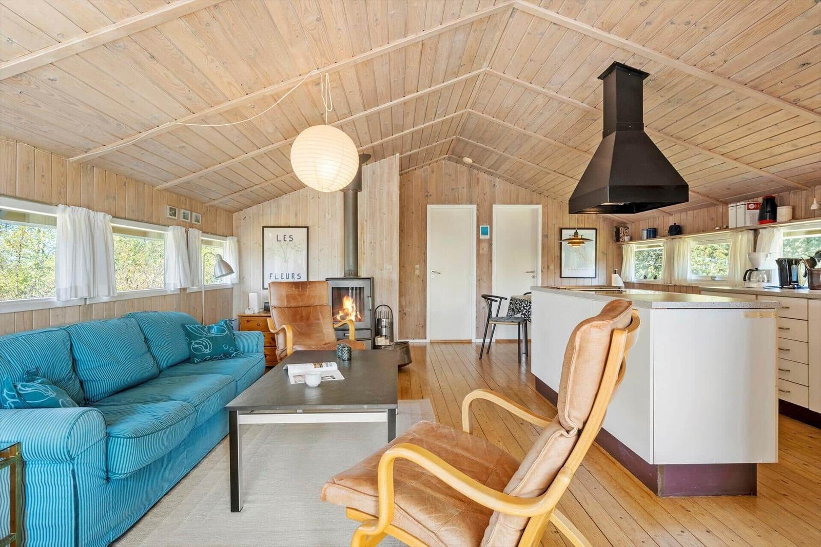 Wohnküche mit Holzdecke, Sofa, Sessel und Kamin.