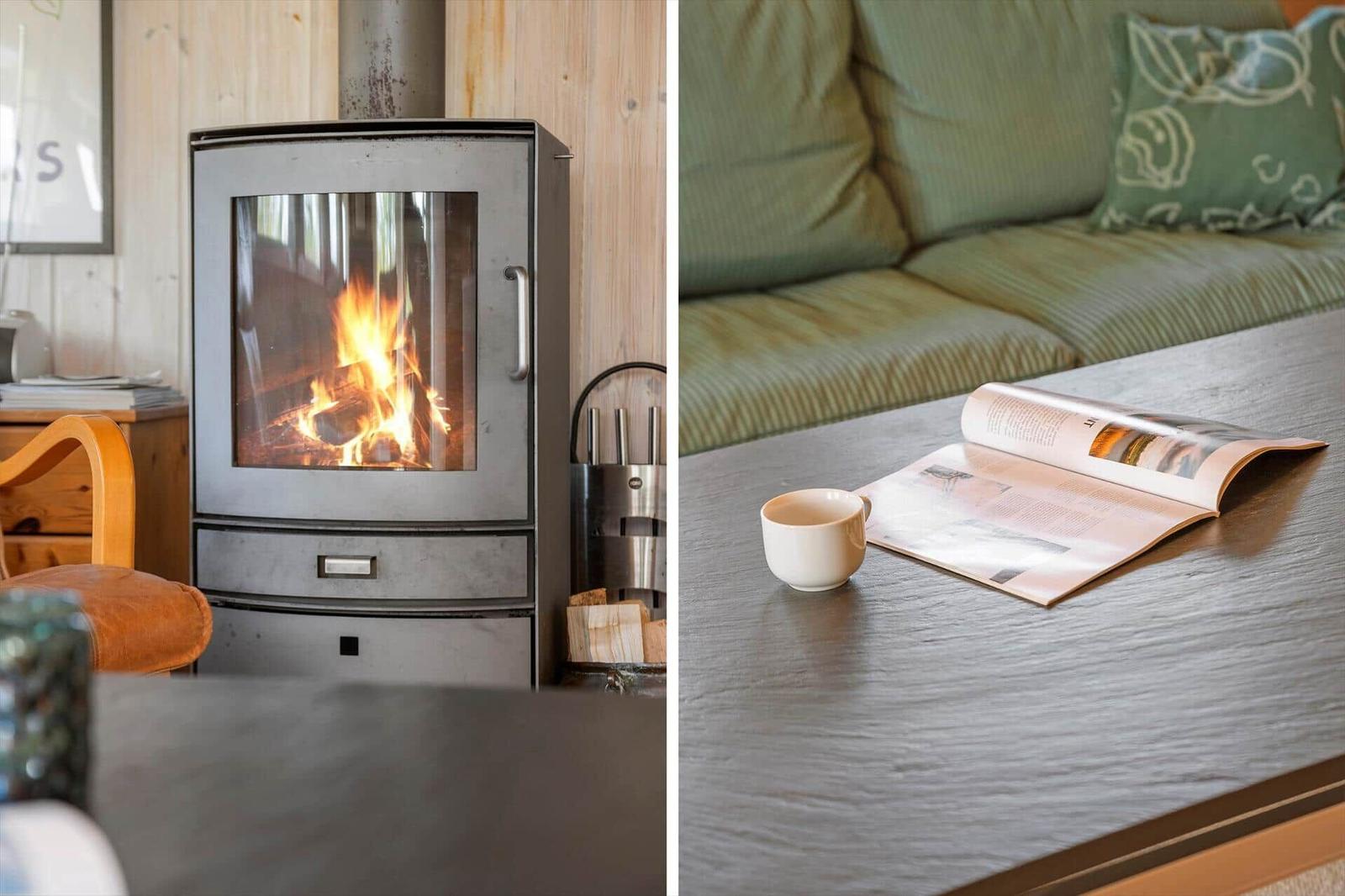 Kamin mit brennendem Holz und Sofa mit Zeitschrift und Tasse.