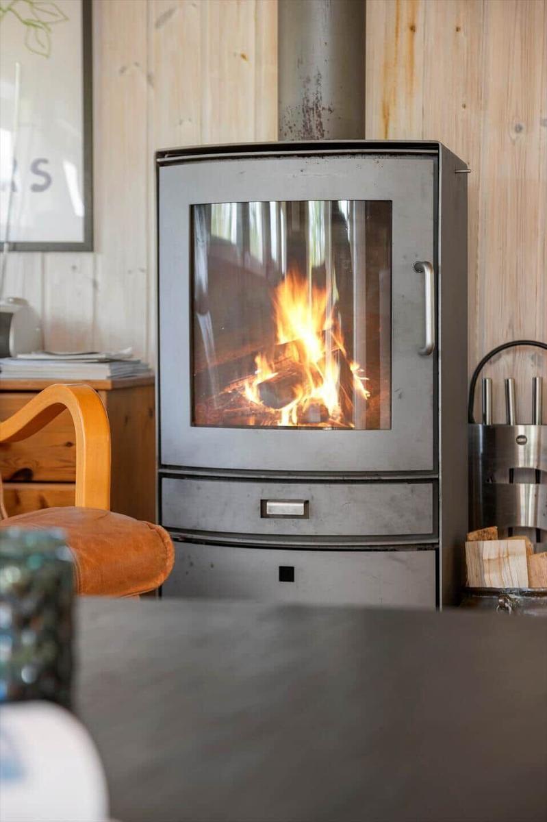 Holzofen mit brennendem Feuer in einem Raum mit Holzwänden und einem Holzstuhl.