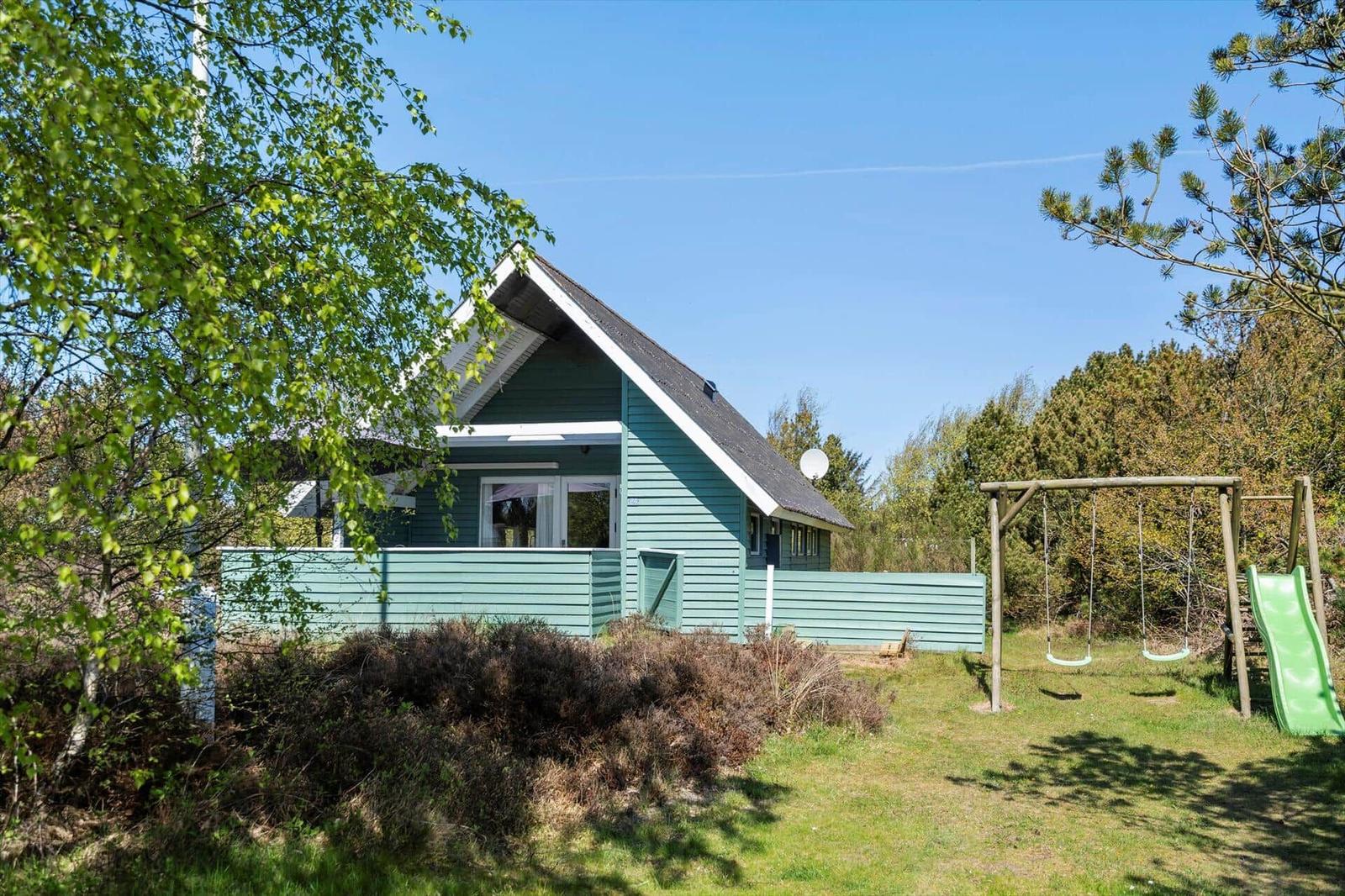 Grünes Ferienhaus mit Spielplatz im Garten unter blauem Himmel