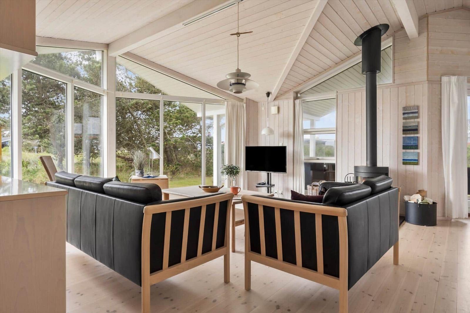 Wohnraum mit zwei schwarzen Ledersofas, Holzdecke und großem Fensterblick auf Grün.