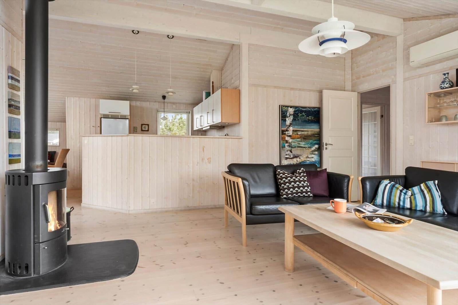 Wohnzimmer mit Kamin, Sofa und Esstisch. Küche im Hintergrund.
