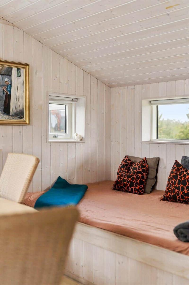 Schlafzimmer mit Holzwand, Bett, Kissen und Fenstern.