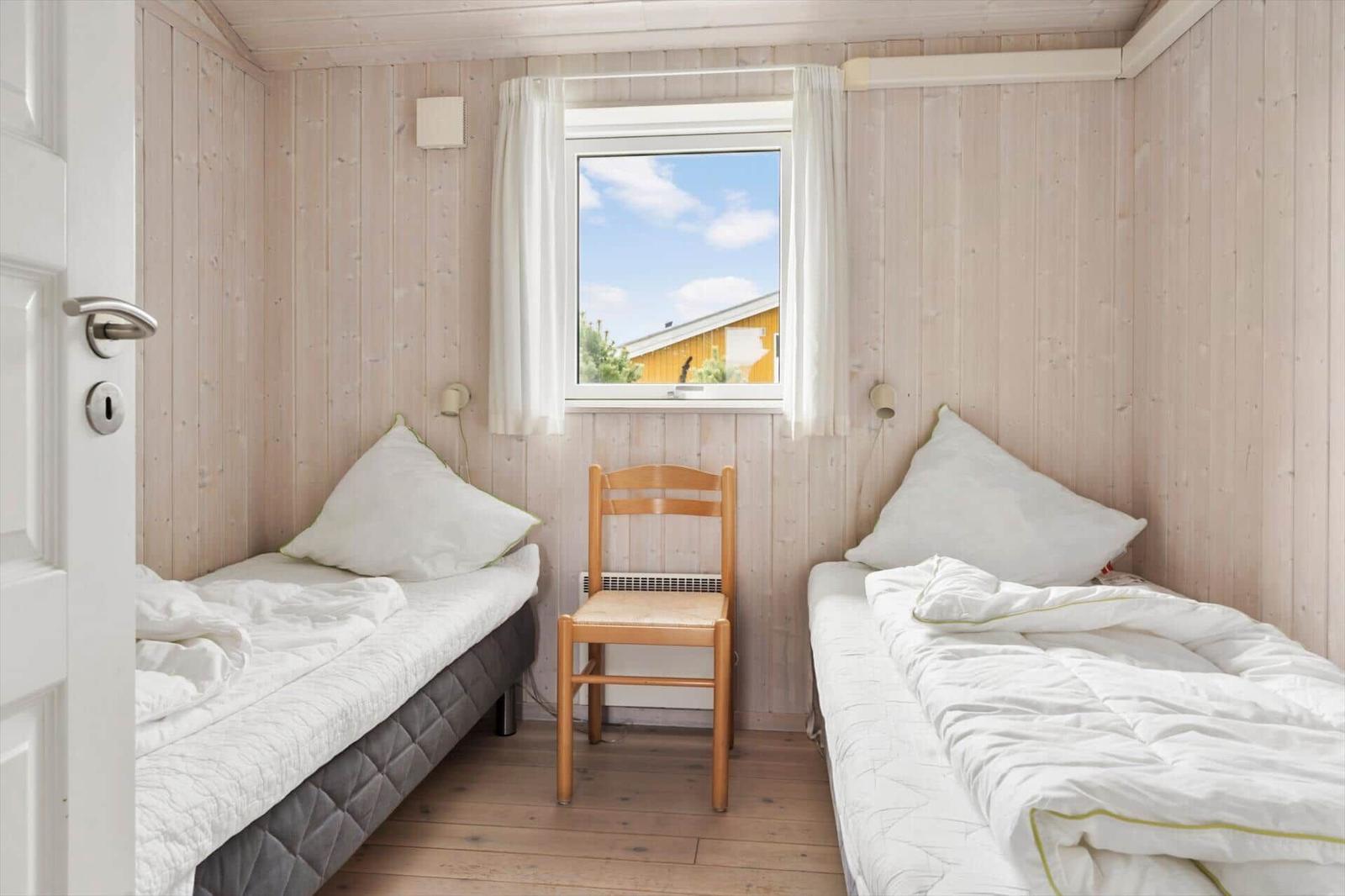 Zwei Einzelbetten mit weißen Bettwäsche, Holzstuhl und Fenster mit Blick nach draußen.