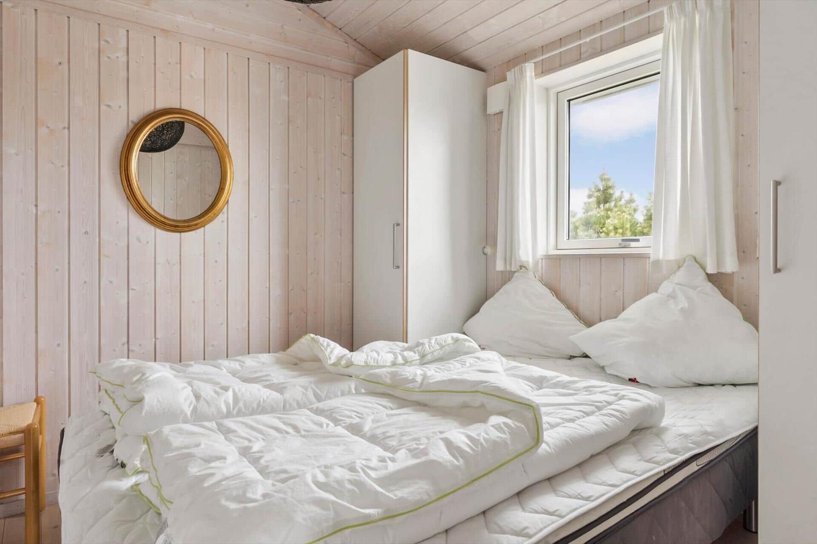 Schlafzimmer mit Bett, Kleiderschrank und Fenster mit Blick auf Bäume.