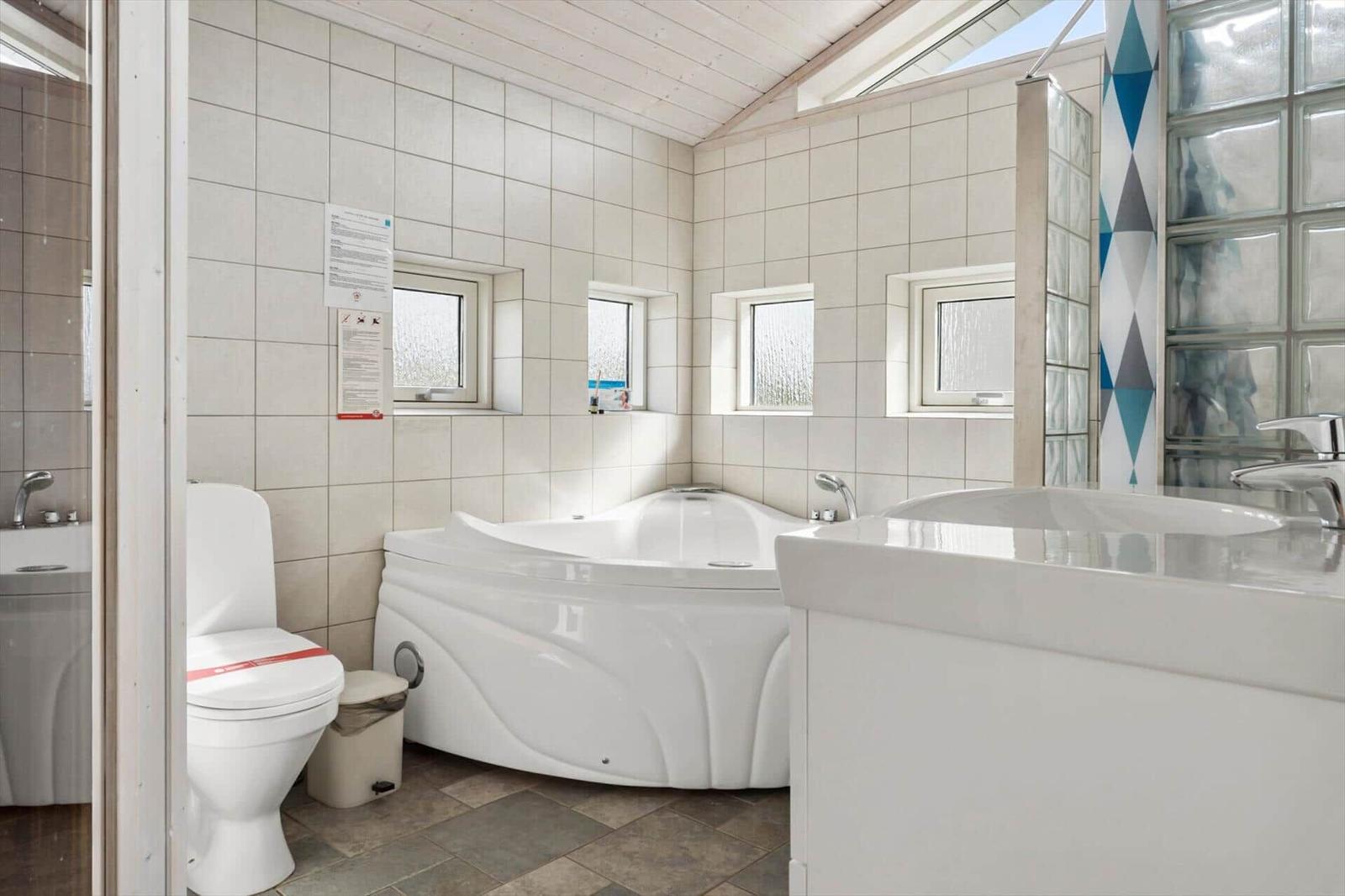 Bad mit Whirlpool, Toilette und Waschbecken. Fenster und Glaswand sorgen für Licht.