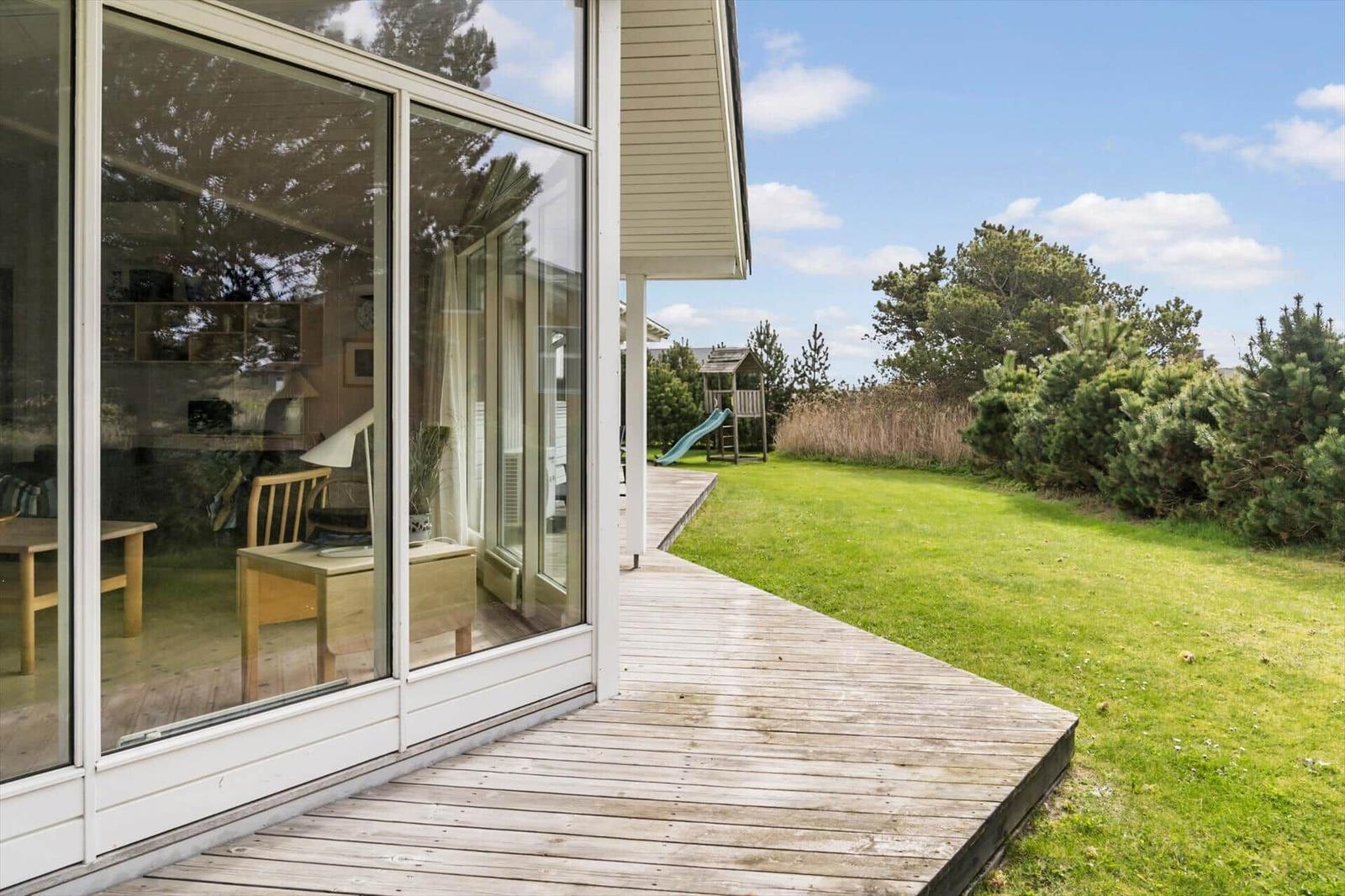 Haus mit Holzterrasse, Glasfront und Garten mit Spielplatz.