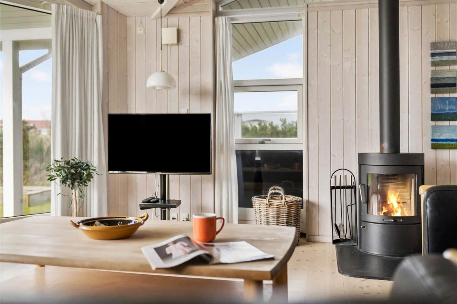 Ein Wohnzimmer mit Holzwänden, Kamin und Fernseher. Auf dem Tisch steht eine Tasse.